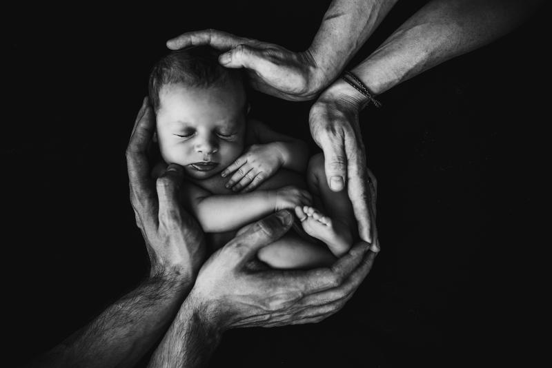 Two pairs of hands holding a baby in the center of an image